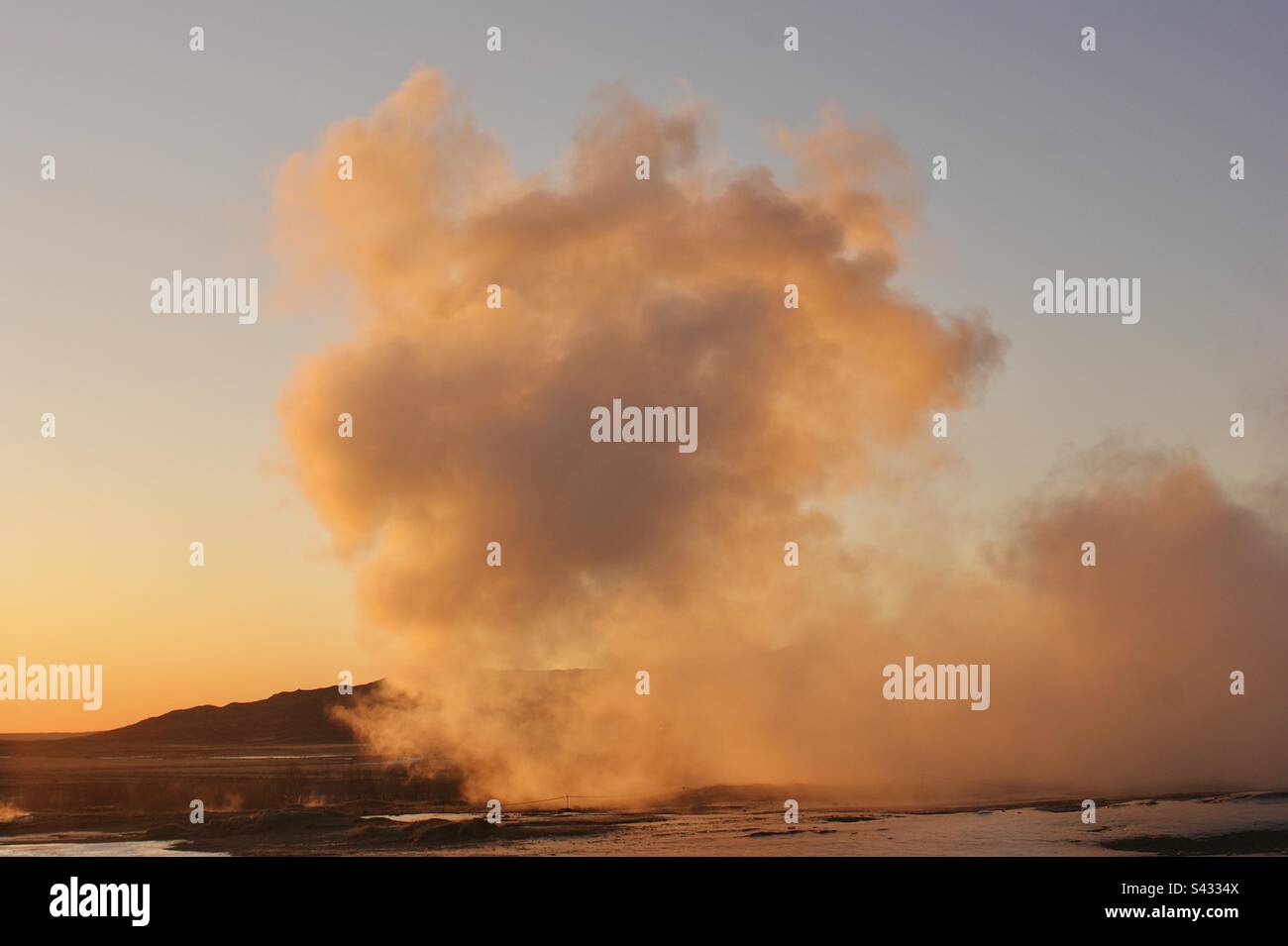 Condensed steam from an Icelandic geyser drifts over the frozen tundra at sunset Stock Photo