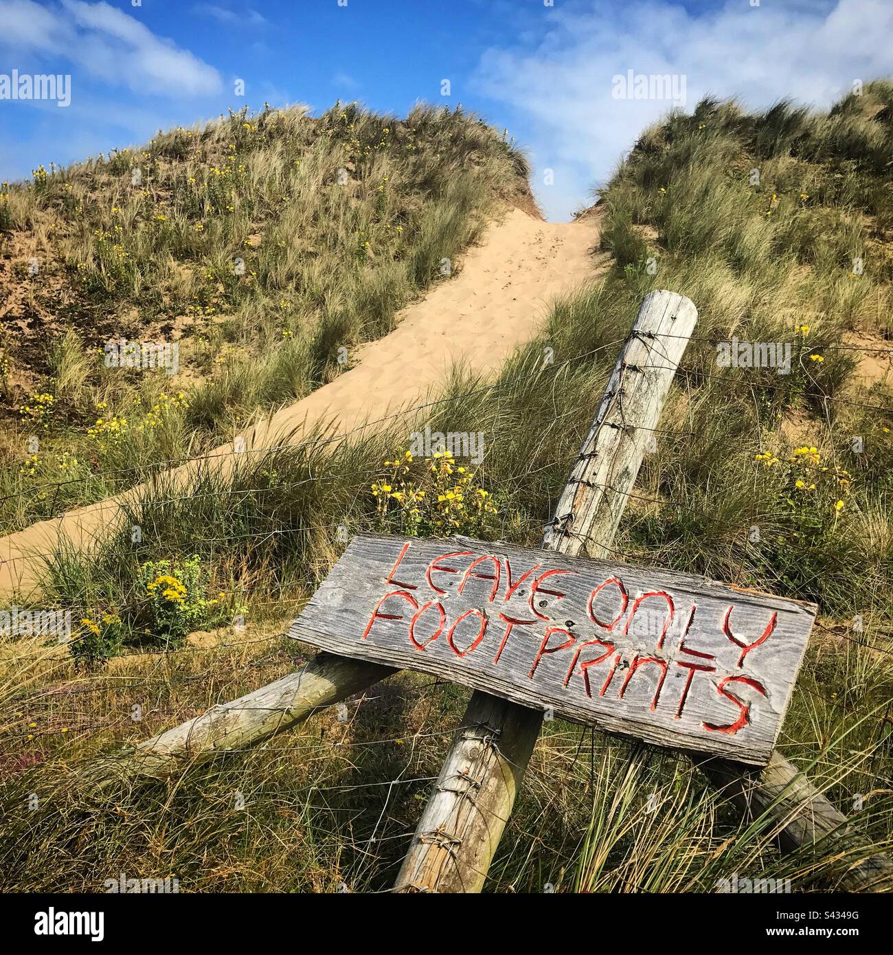 An imaginative sign stating ’leave only footprints’ on a path in the sand dunes of the public beach at Llangennith near Rhossili in the Gower area of West Wales Stock Photo