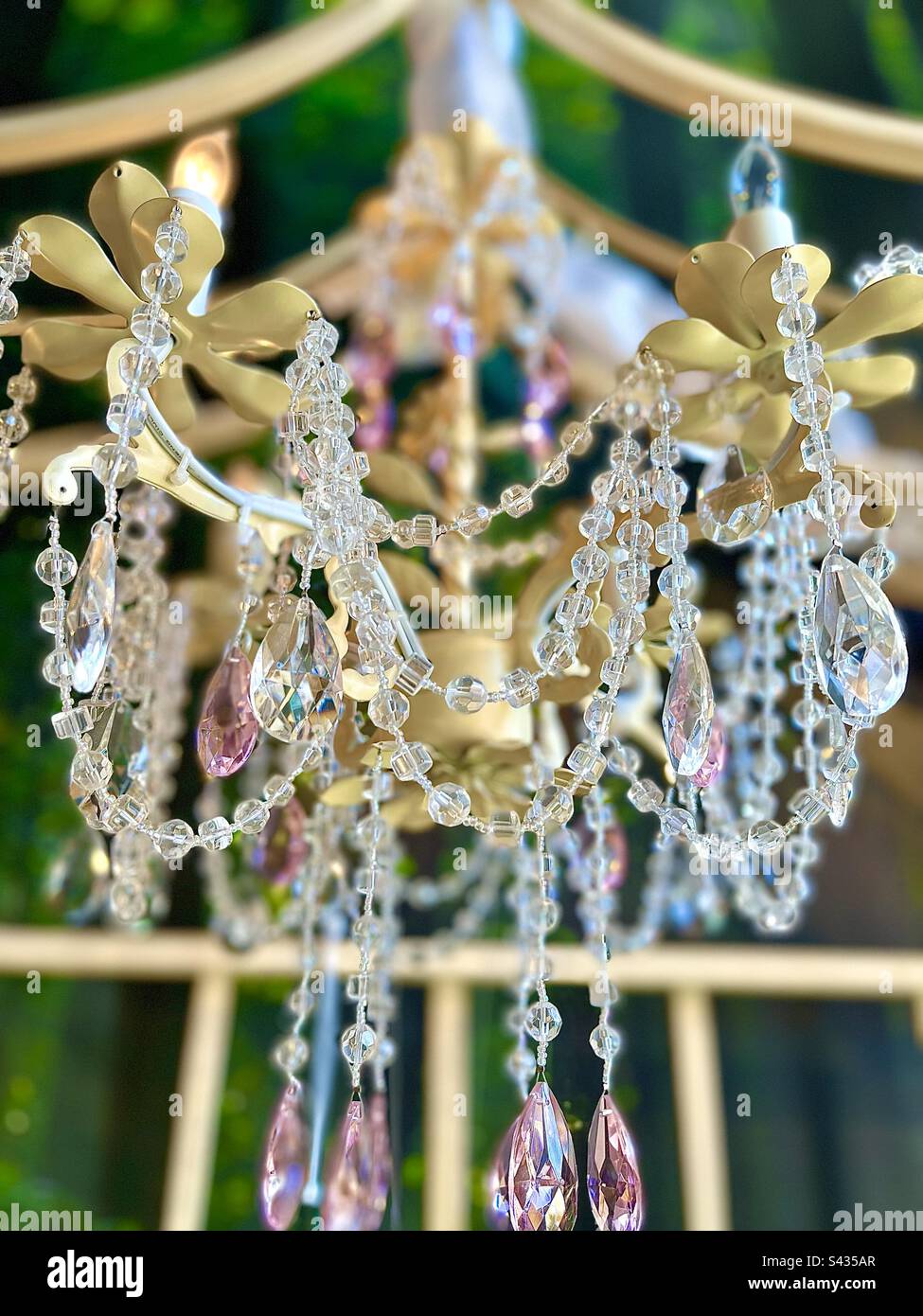 Gold chandelier with pink and crystal beads against lush green natural background. - Smartphone Captured Stock Image