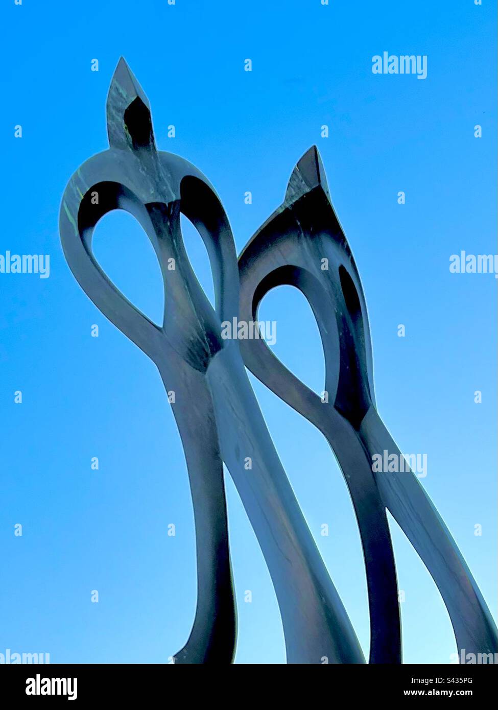 Larger Than Life. Black marble sculpture of two human figures posing proudly in front of clear bright blue sky. Includes print space. Stock Photo