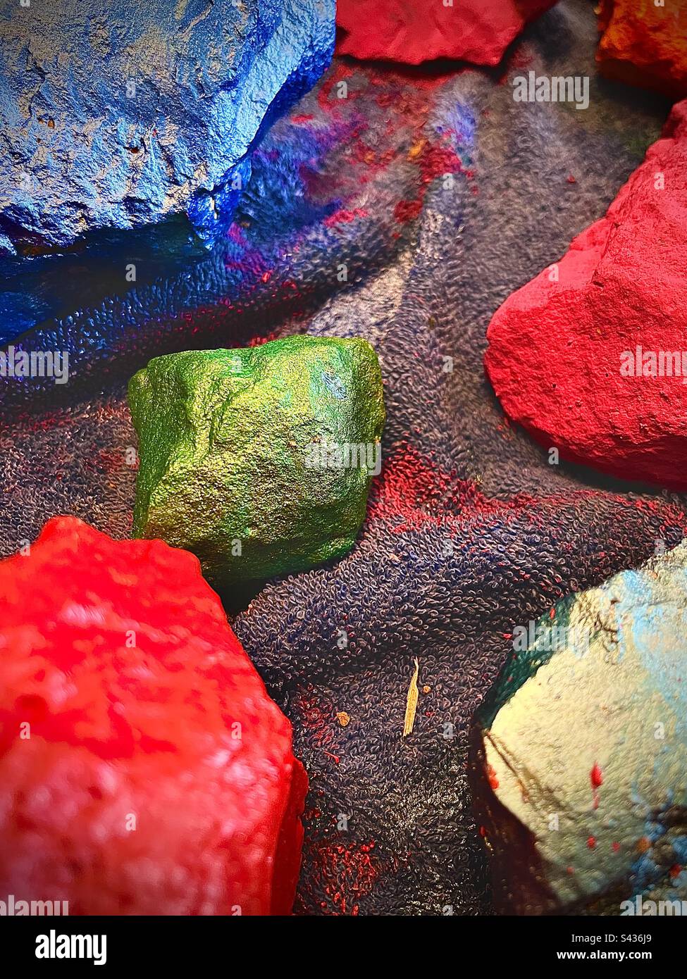 Richly textured rocks painted in vibrant solid colors on messy paint