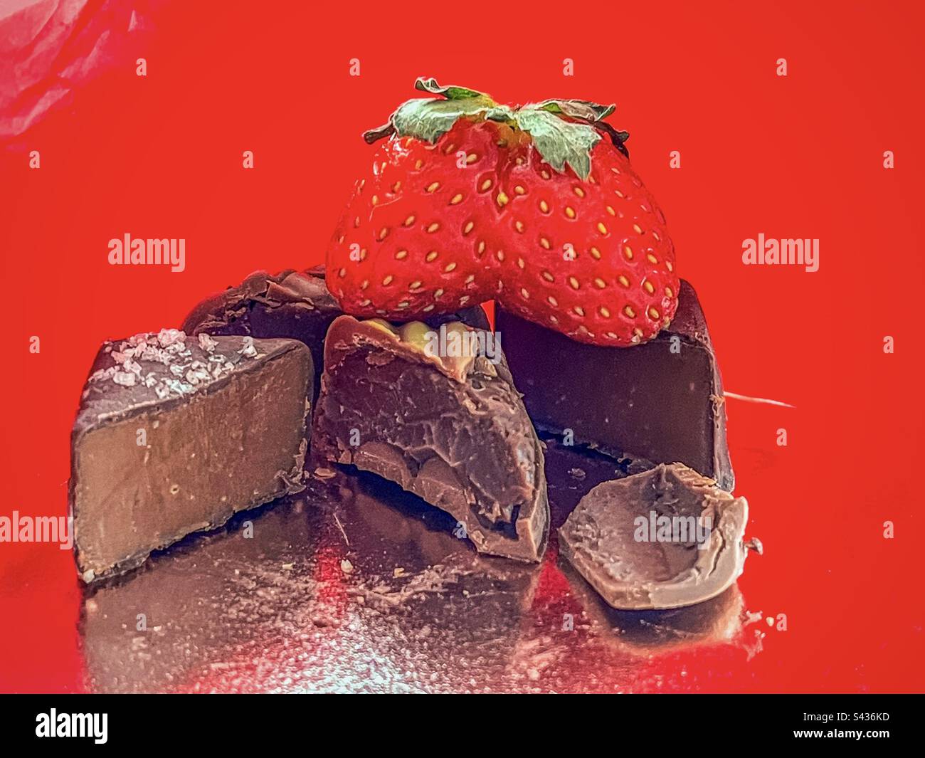 Close-up of fused strawberry on top of dark caramel chocolate and honey praline chocolate on red, reflective background. - Smartphone Captured Stock Image