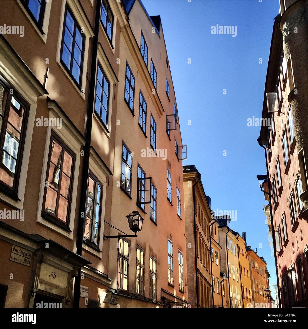 The beautiful shadowy orange and yellow painted exteriors of traditional buildings on the narrow streets of Stockholm Old Town Gamla Stan in Sweden under a clear blue sky - Smartphone Captured Stock Image