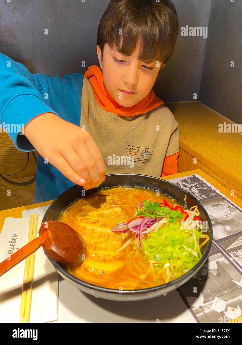 A boy eating a bowl of chilli ramen noodles with chicken and broth in a restaurant. - Smartphone Captured Stock Image