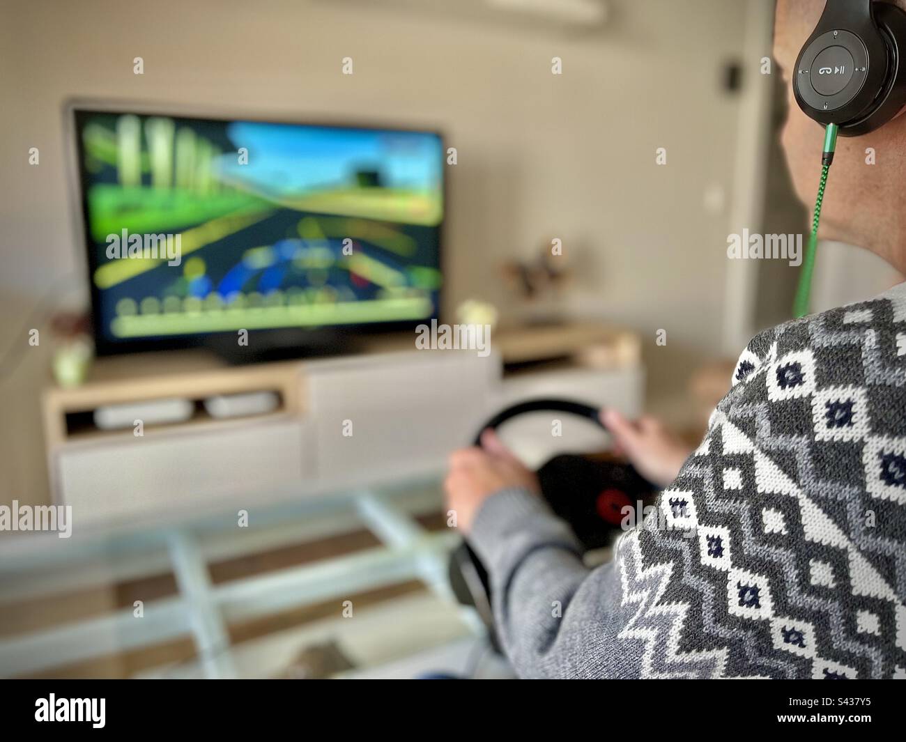Man playing a video game at home, driving with a steering wheel a race
