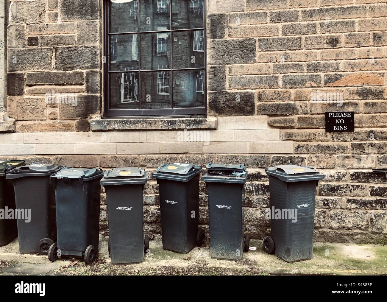 A row of rubbish bins in a lane next to a sign saying Please No Bins in an alley in Edinburgh, Scotland, United Kingdom Stock Photo