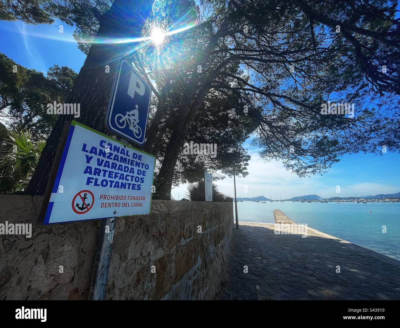 No anchor sign and jetty with tree on the seafront. Bay of Pollença, Mallorca. Sign reads: “CANAL DE LANZAMIENTO Y VARADA DE ARTEFACTOS FLOTANTES” Stock Photo