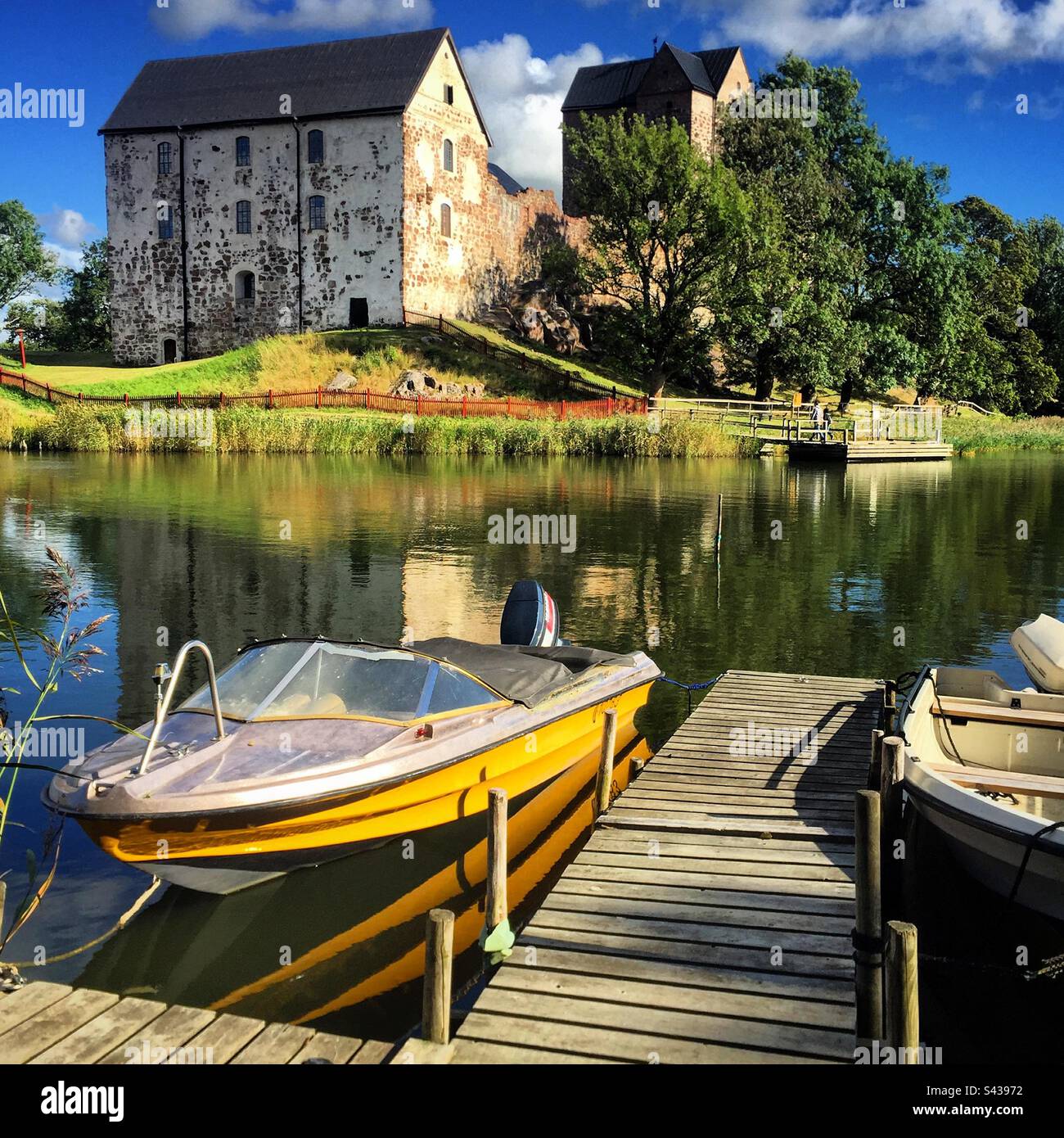 A speedboat at a lake pier next to the beautiful ancient castle of Kastelholm in the Åland Islands archipelago in the Baltic Sea region of Finland in summer. - Smartphone Captured Stock Image A speedboat at a lake pier next to the beautiful ancient castle of Kastelholm in the Åland Islands archipelago in the Baltic Sea region of Finland in summer. - Smartphone Captured Stock Image