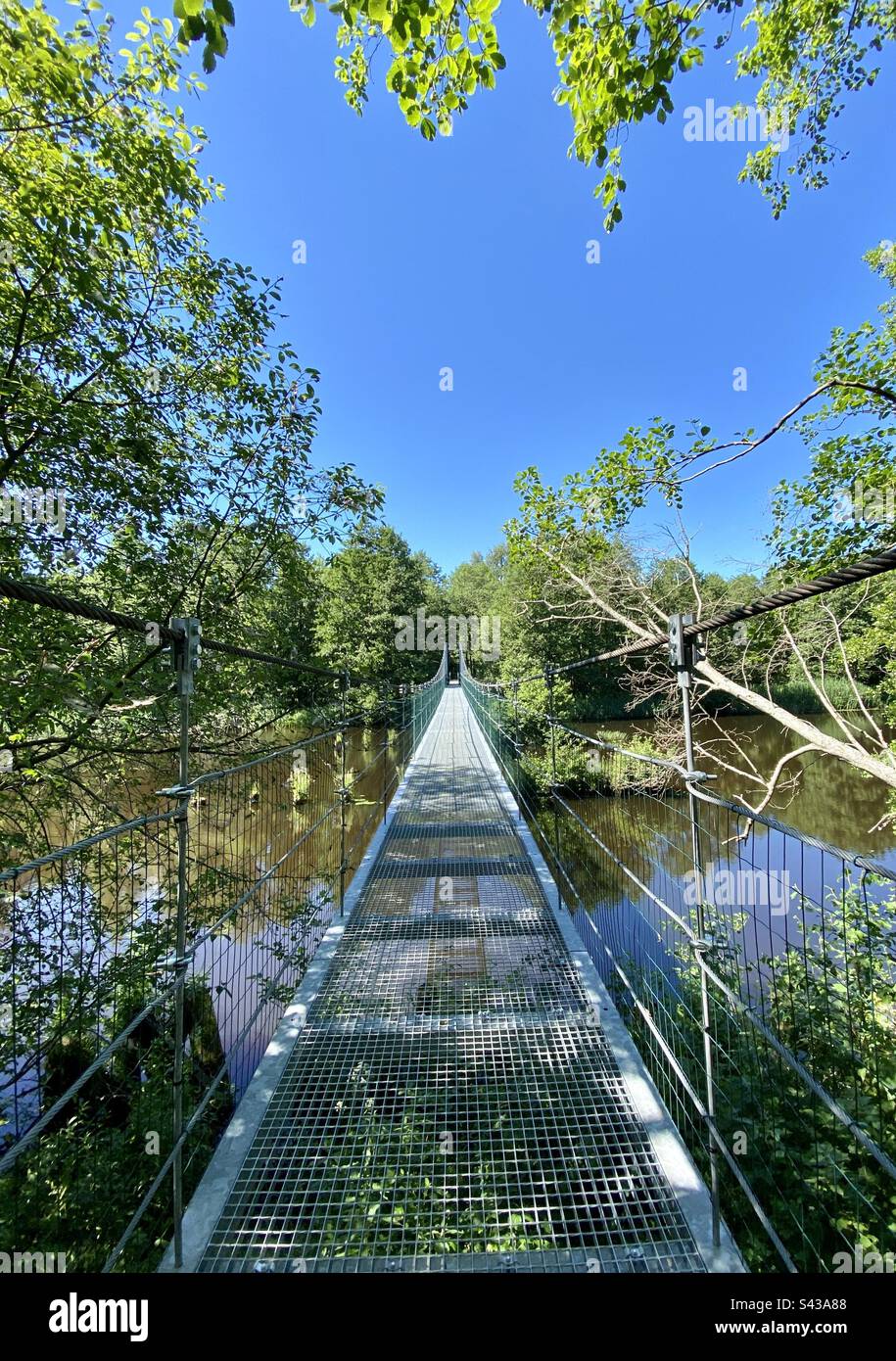 Wide angle shot of a walkers bridge over river Irbe in Kurzeme, Latvia on a sunny and warm summer day. Stock Photo