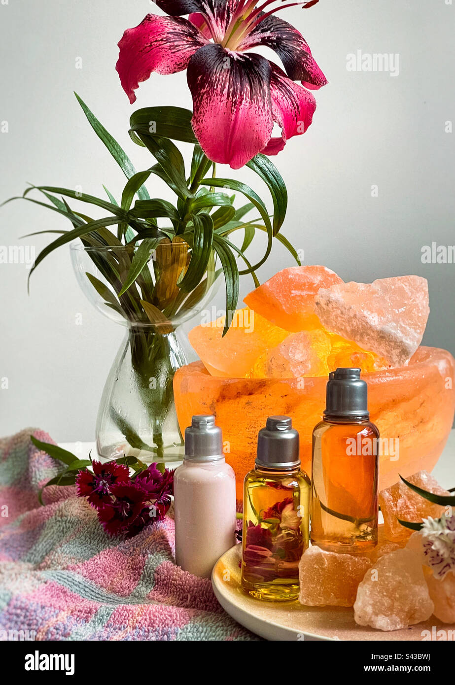 Spa concept arrangement of toiletries bottles, rock crystals, salt lamp, fresh flowers and towel on table. - Smartphone Captured Stock Image