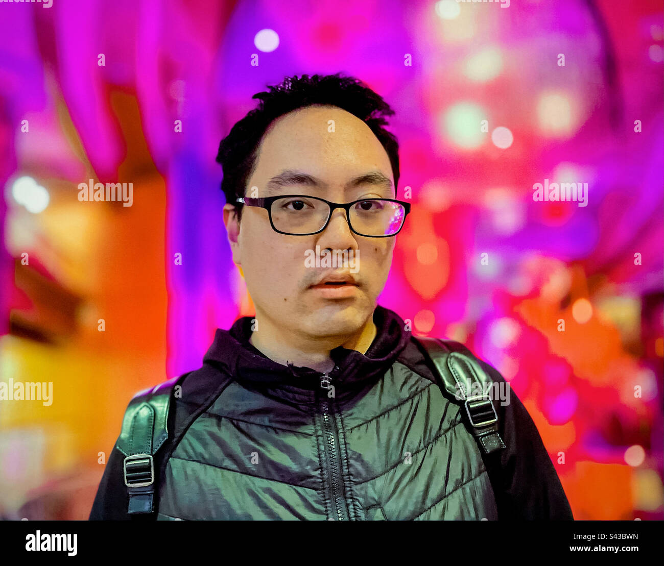 Portrait of young Asian man in eyeglasses against colorful, illuminated, nightlife defocused background. - Smartphone Captured Stock Image
