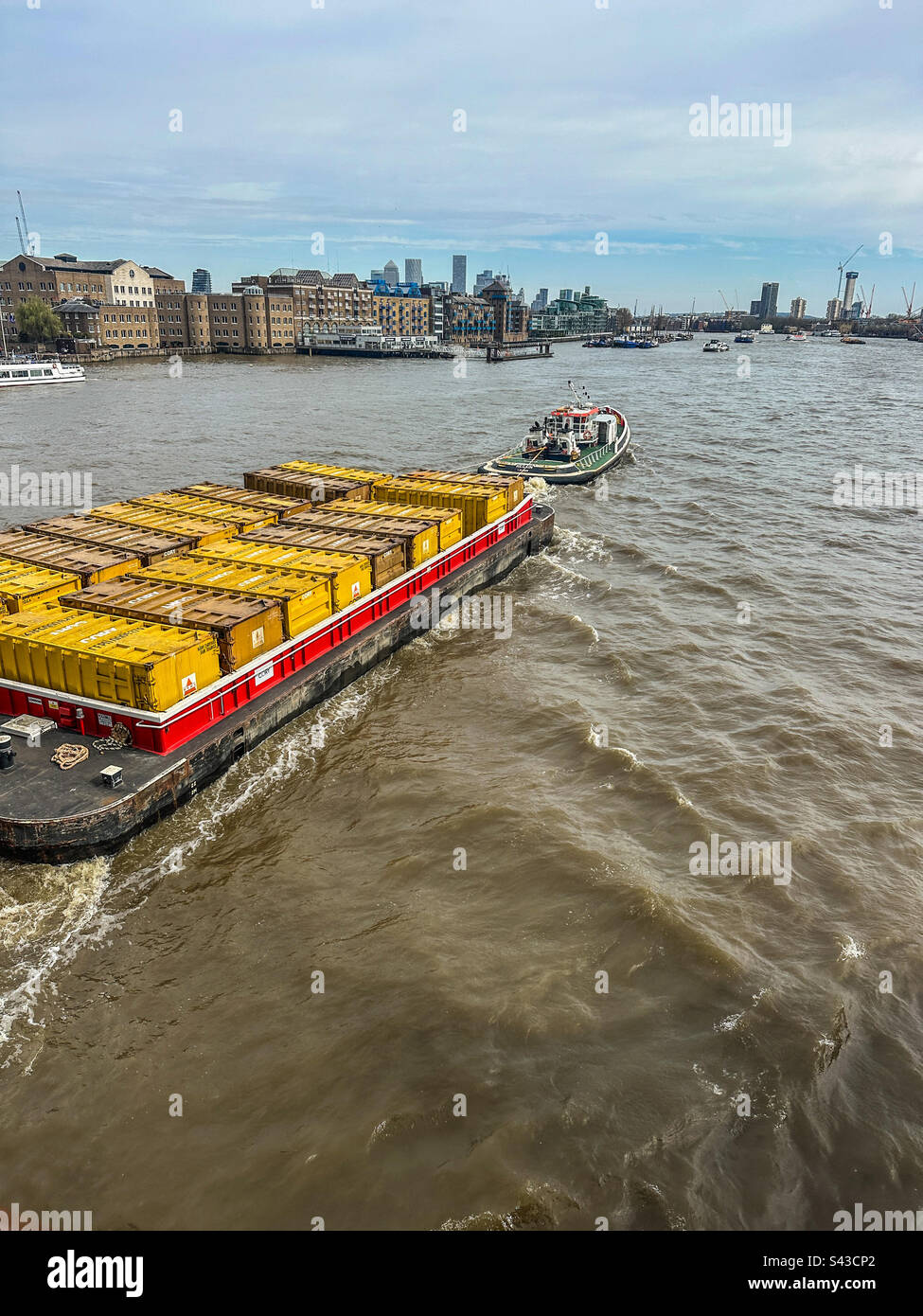 Tug boat pulling large barge loaded with yellow shipping containers on the River Thames, London, England Stock Photo