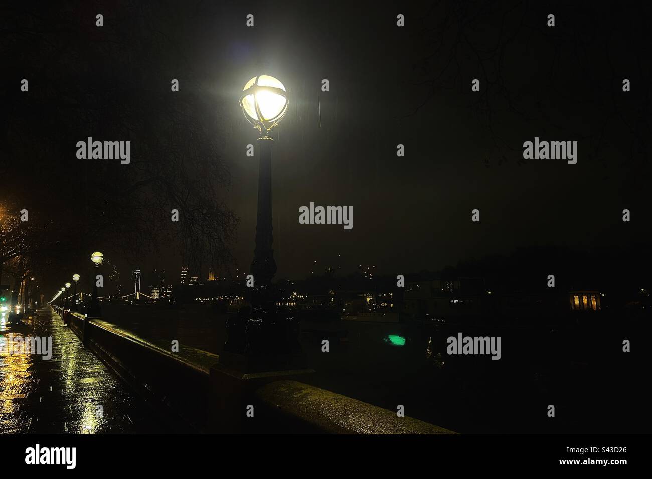 Street lamps shine brightly on the Albert Embankment on the Thames Path in London at night - heritage lamps line the banks of the Thames many by Suggs & Co Stock Photo