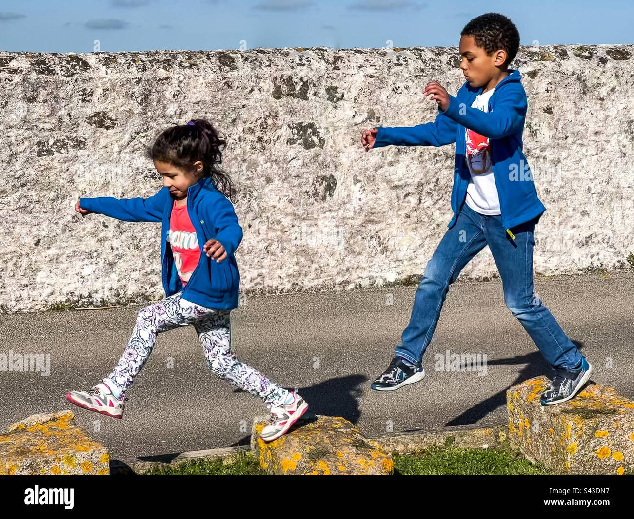 Mixed race brother and sister jumping between large stones - Smartphone Captured Stock Image