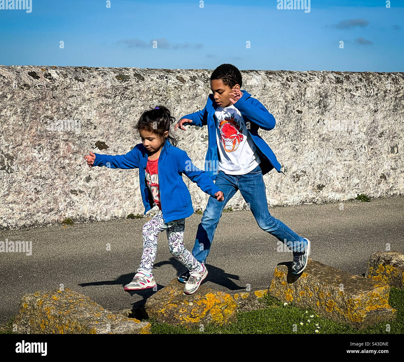 Mixed race brother and sister jumping between stone blocks. - Smartphone Captured Stock Image