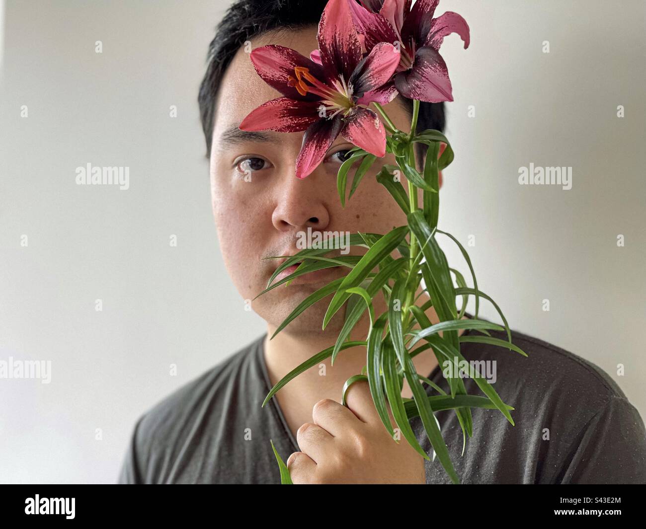 Close-up portrait of young Asian man holding red lilies on white background. - Smartphone Captured Stock Image