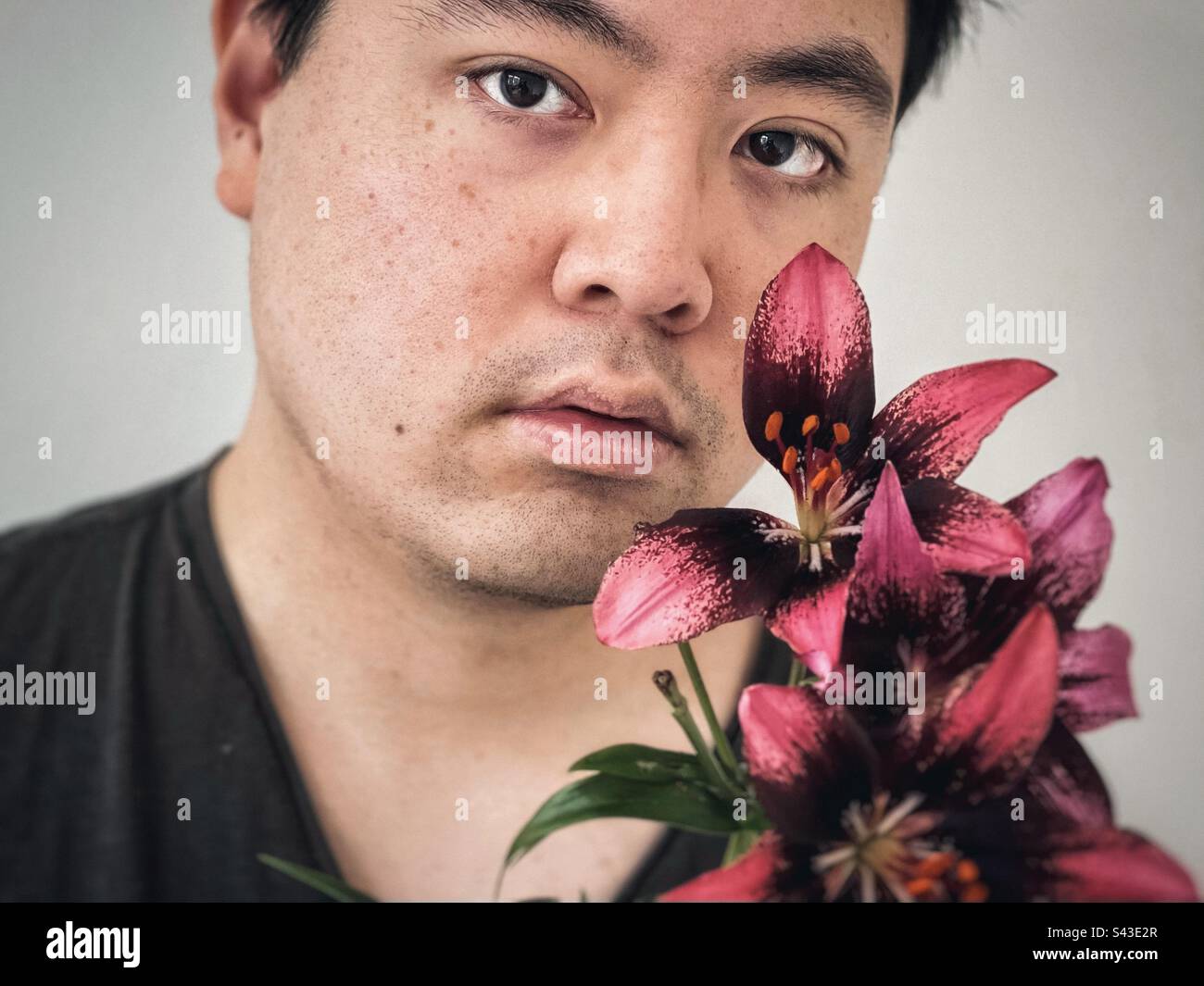 Headshot of young Asian man with red lilies on white background. - Smartphone Captured Stock Image