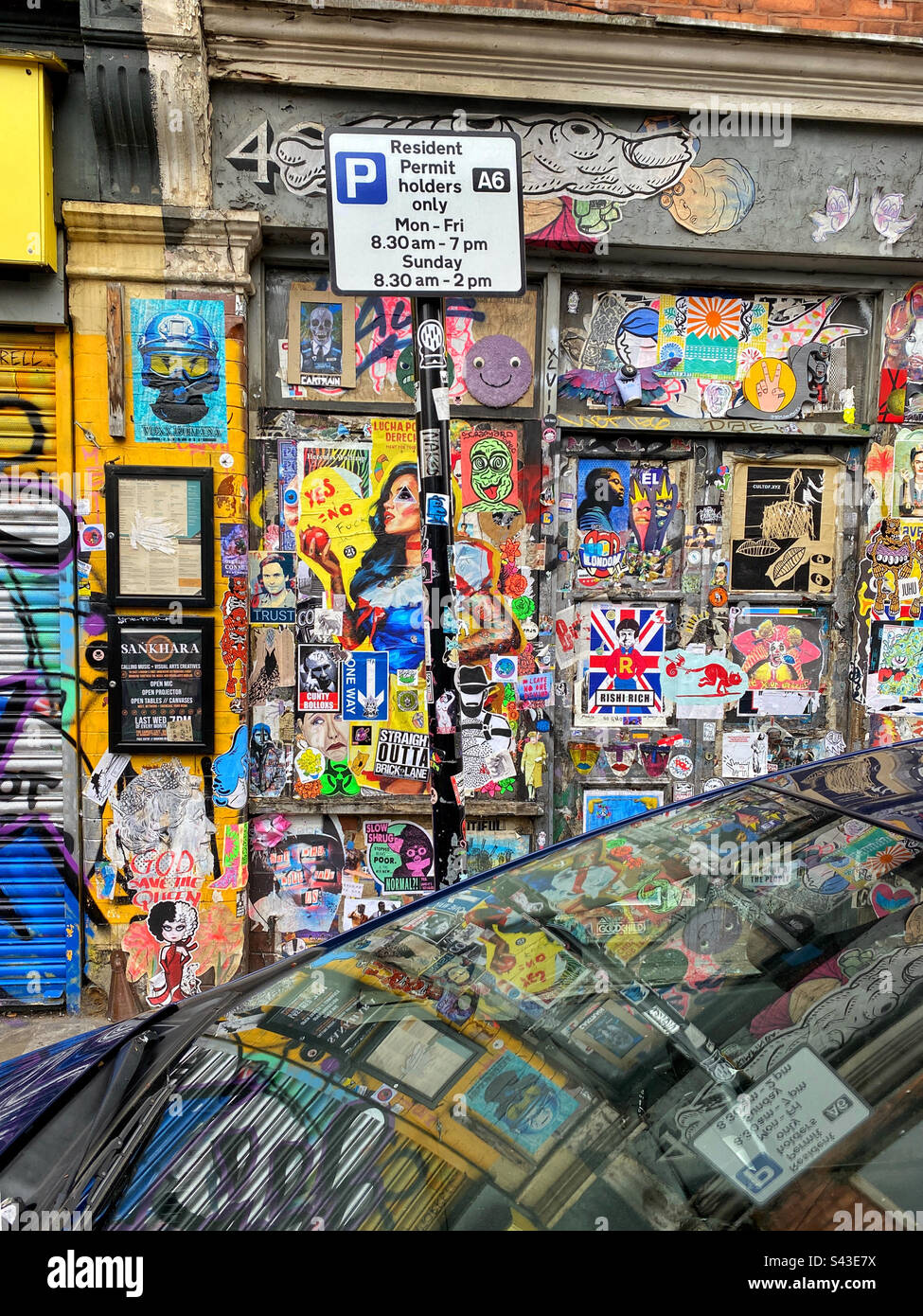 A colourful street scene from the Brick Lane area of London. Lots of adverts, posters and graffiti adorn the walls and are reflected in a car windshield. Is this streetart? Photo ©️ COLIN HOSKINS. - Smartphone Captured Stock Image