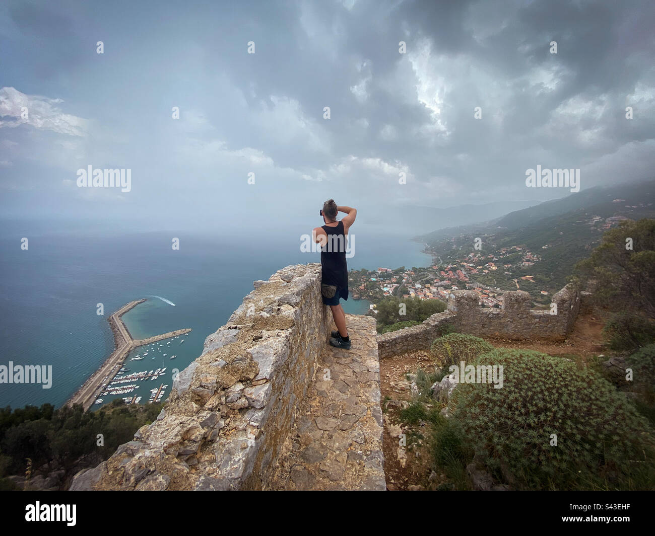 Man taking photo of incredible view with phone, standing on ancient stone wall, Rocca di Cefalù, Sicily. - Smartphone Captured Stock Image