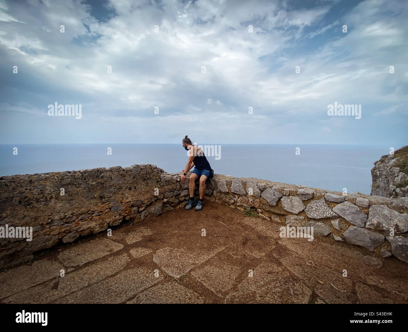 Man sitting on stone wall, looking over cliff. - Smartphone Captured Stock Image