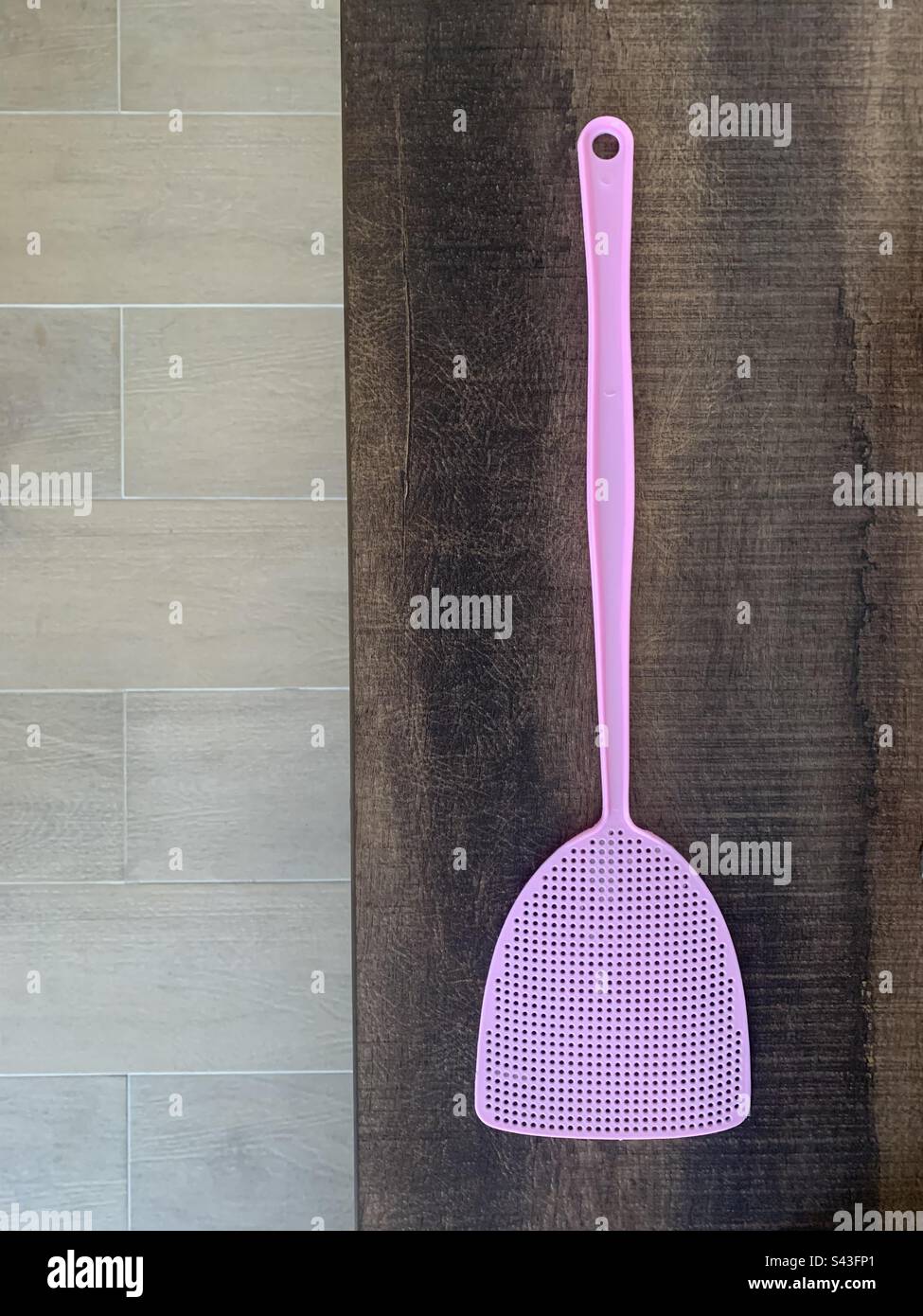 Pastel pink fly swatter on top of a dark brown sideboard cabinet - Smartphone Captured Stock Image
