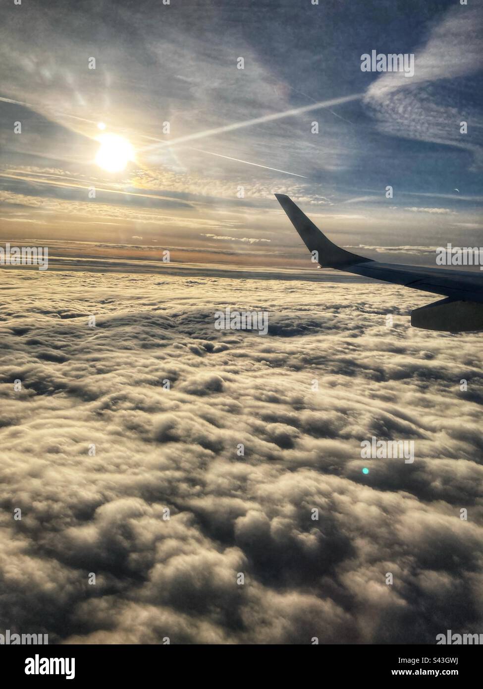 View on the left wing on a plane over the clouds with the sun in the background - Smartphone Captured Stock Image