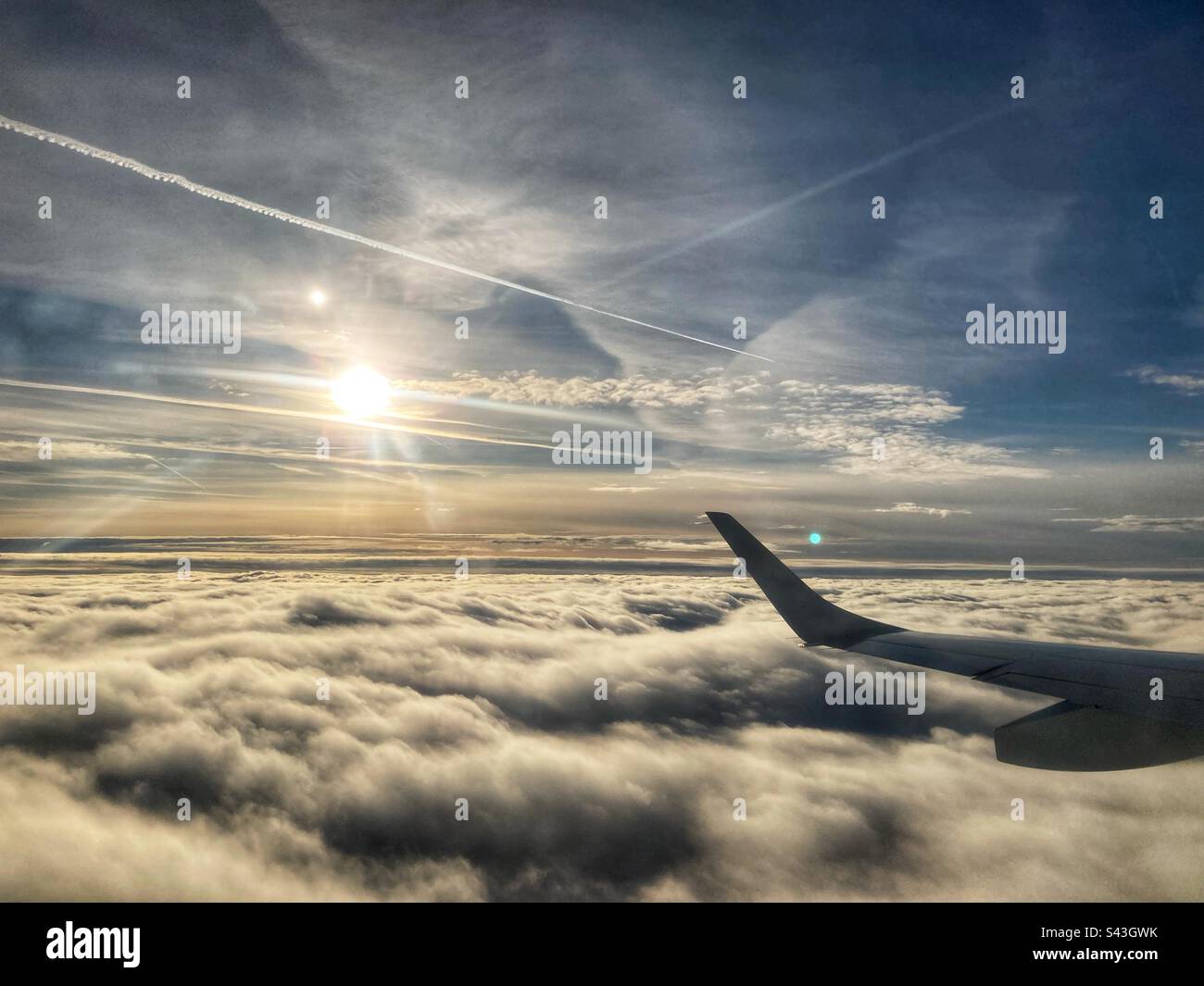 View on the left wing on a plane over the clouds with the sun in the background - Smartphone Captured Stock Image