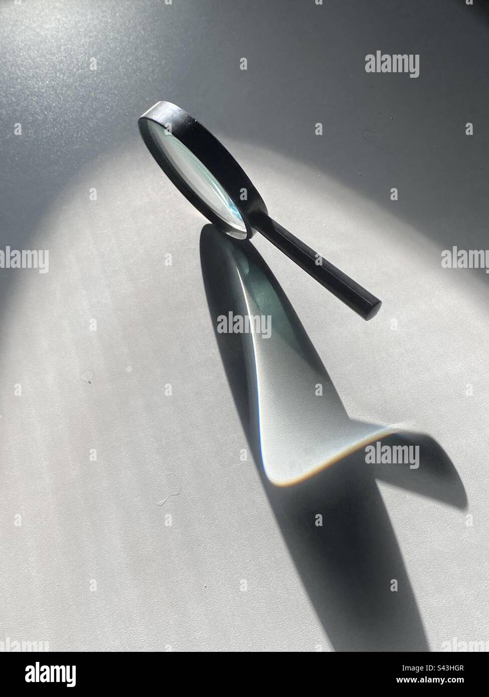 A magnifying glass casts a curvature with the lens on a counter in bright sunlight - Smartphone Captured Stock Image