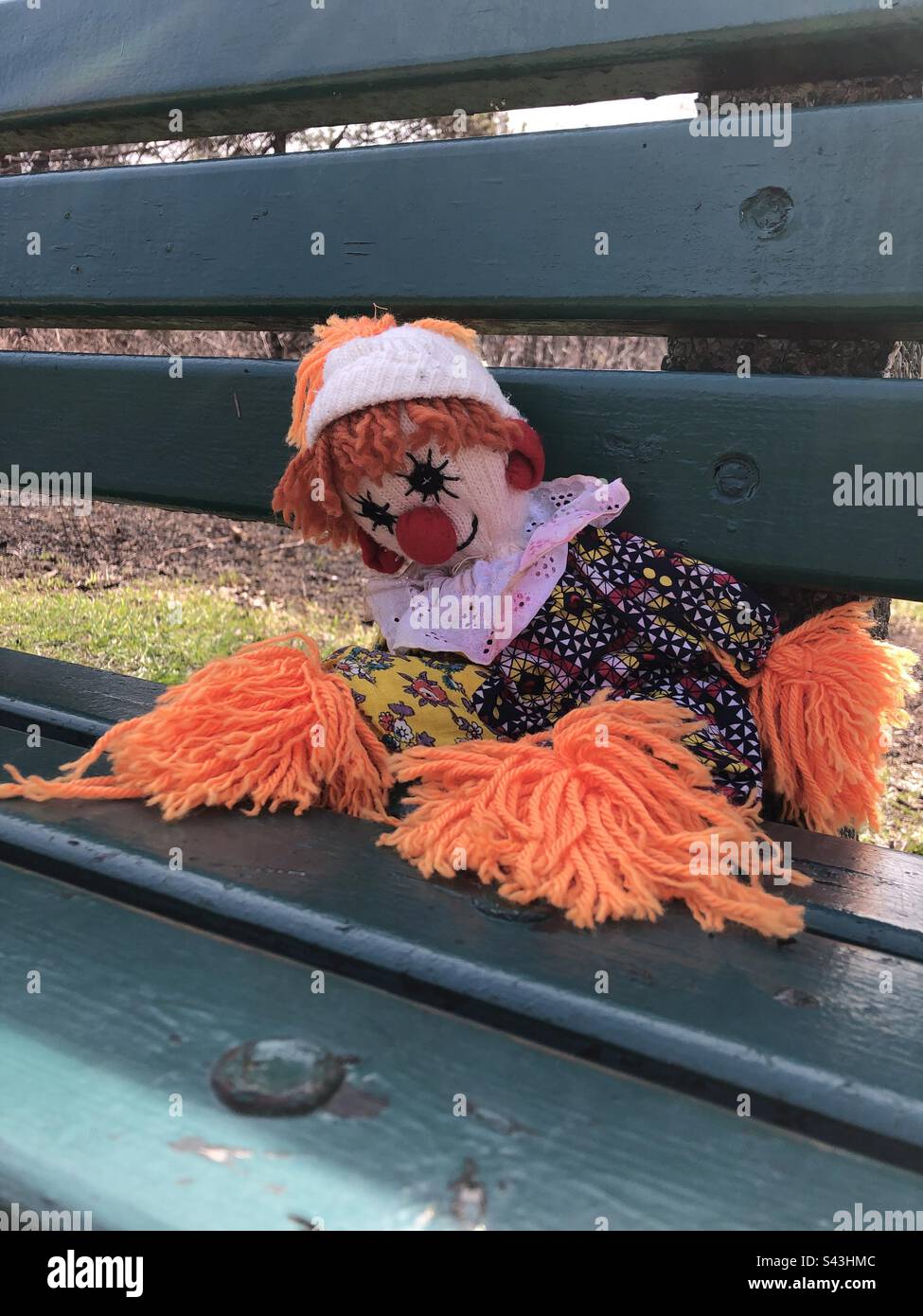 Clown doll sitting on a park bench. Stock Photo