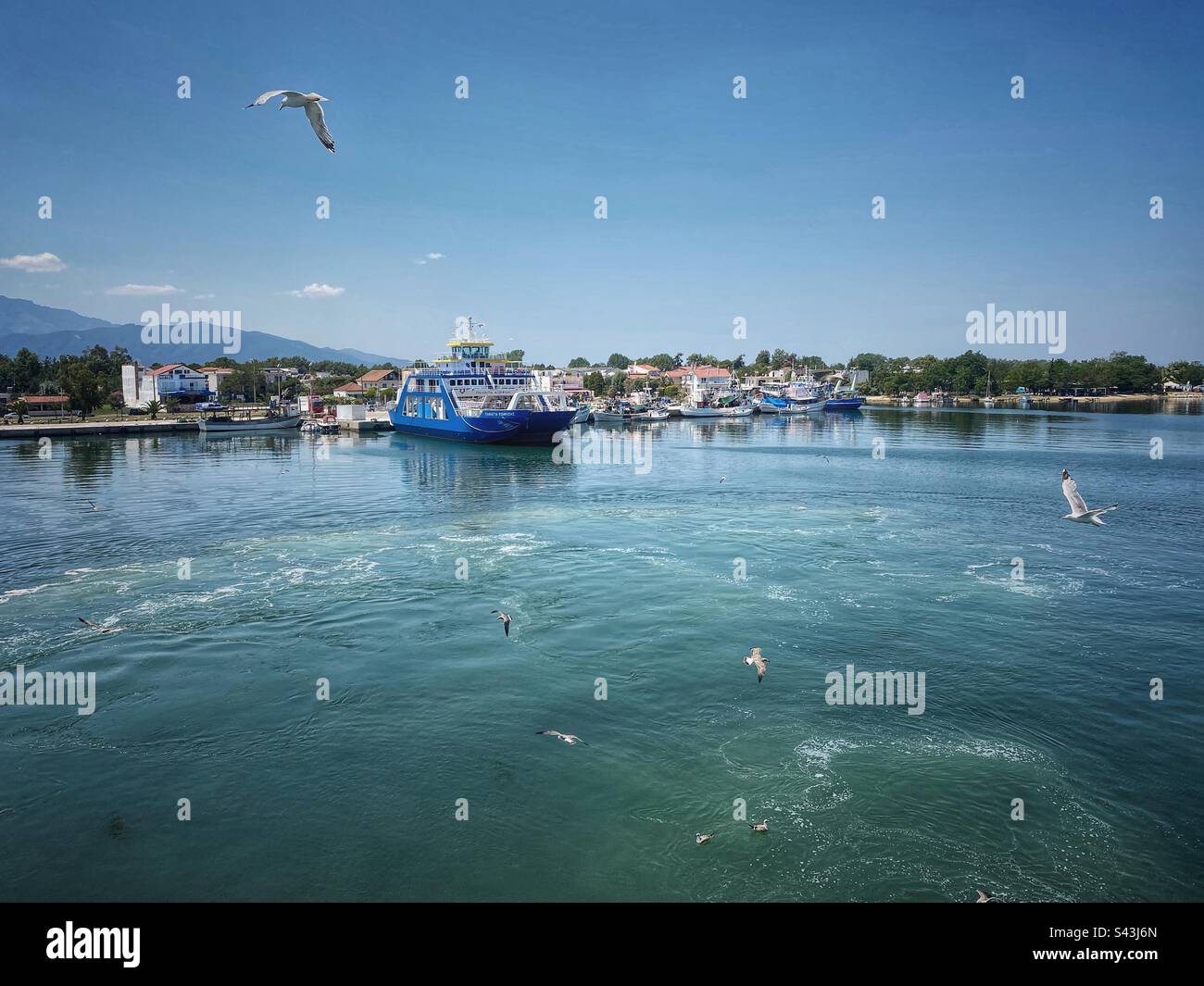 Port view from the sea with ferry boat and flying seagulls in Keramoti town in Greece. - Smartphone Captured Stock Image