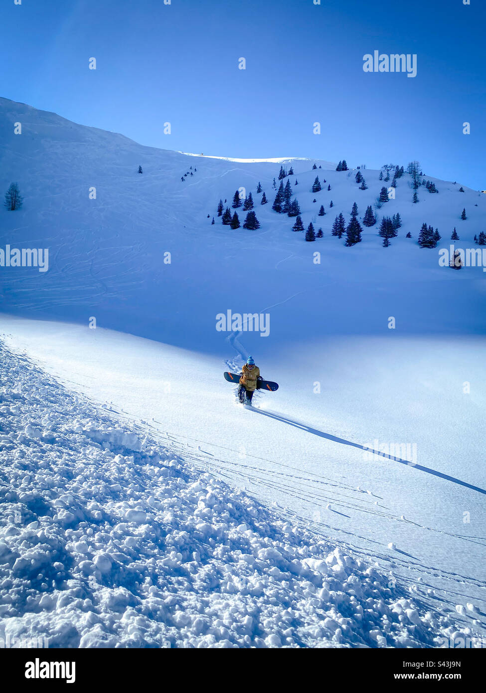 Snowboarder walking through deep powder on a sunny slope. - Smartphone Captured Stock Image