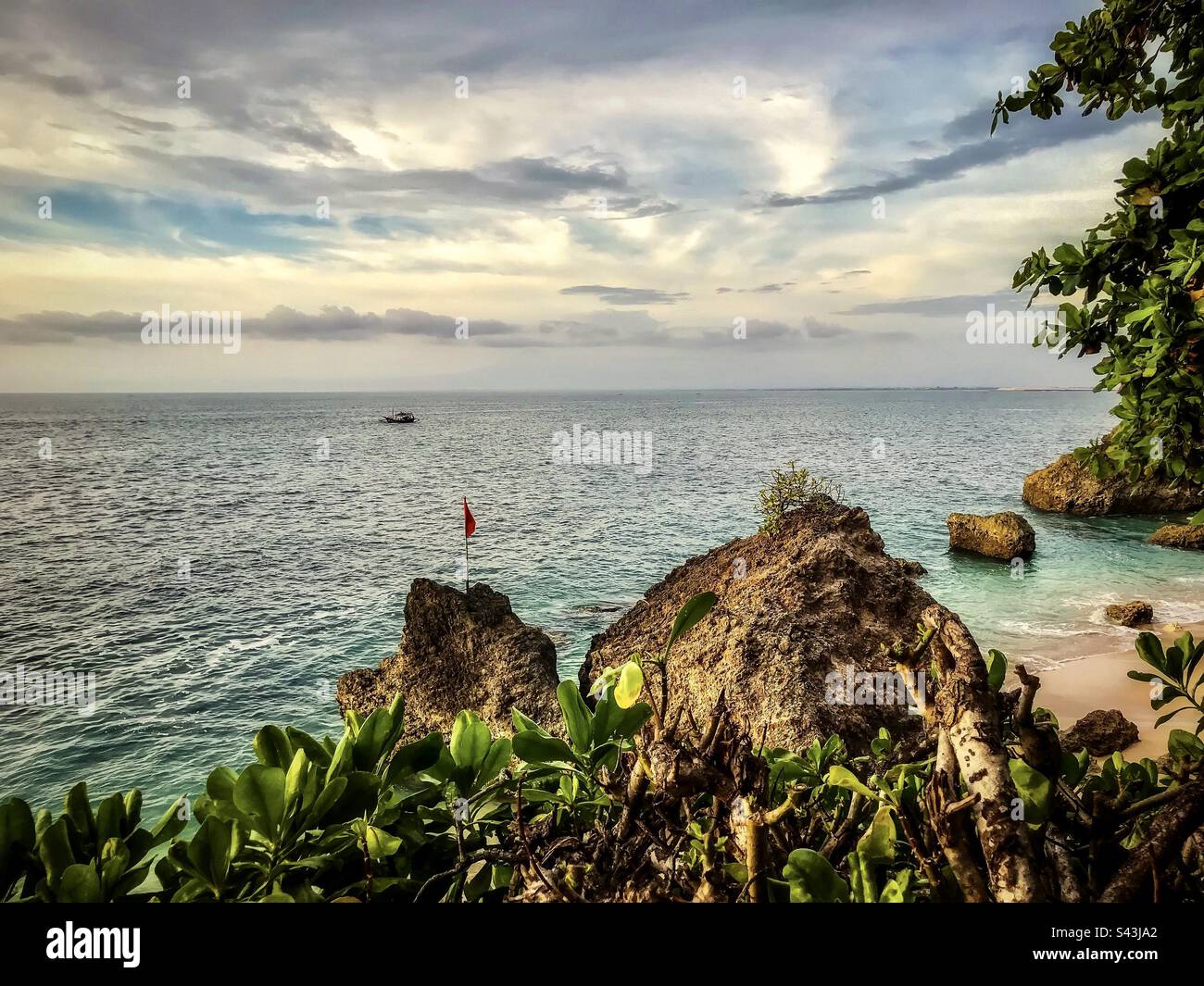 Scenic view of rocky beach, sea, boat and sky in Jimbaran, Bali, Indonesia. - Smartphone Captured Stock Image