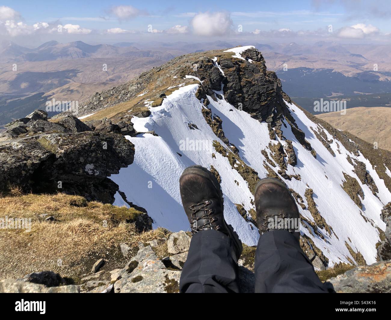 A Walker wearing a pair of leather boots on the summit of Ben Lui, with a view of Coire Gaothach holding the snow, Tyndrum Scotland Stock Photo