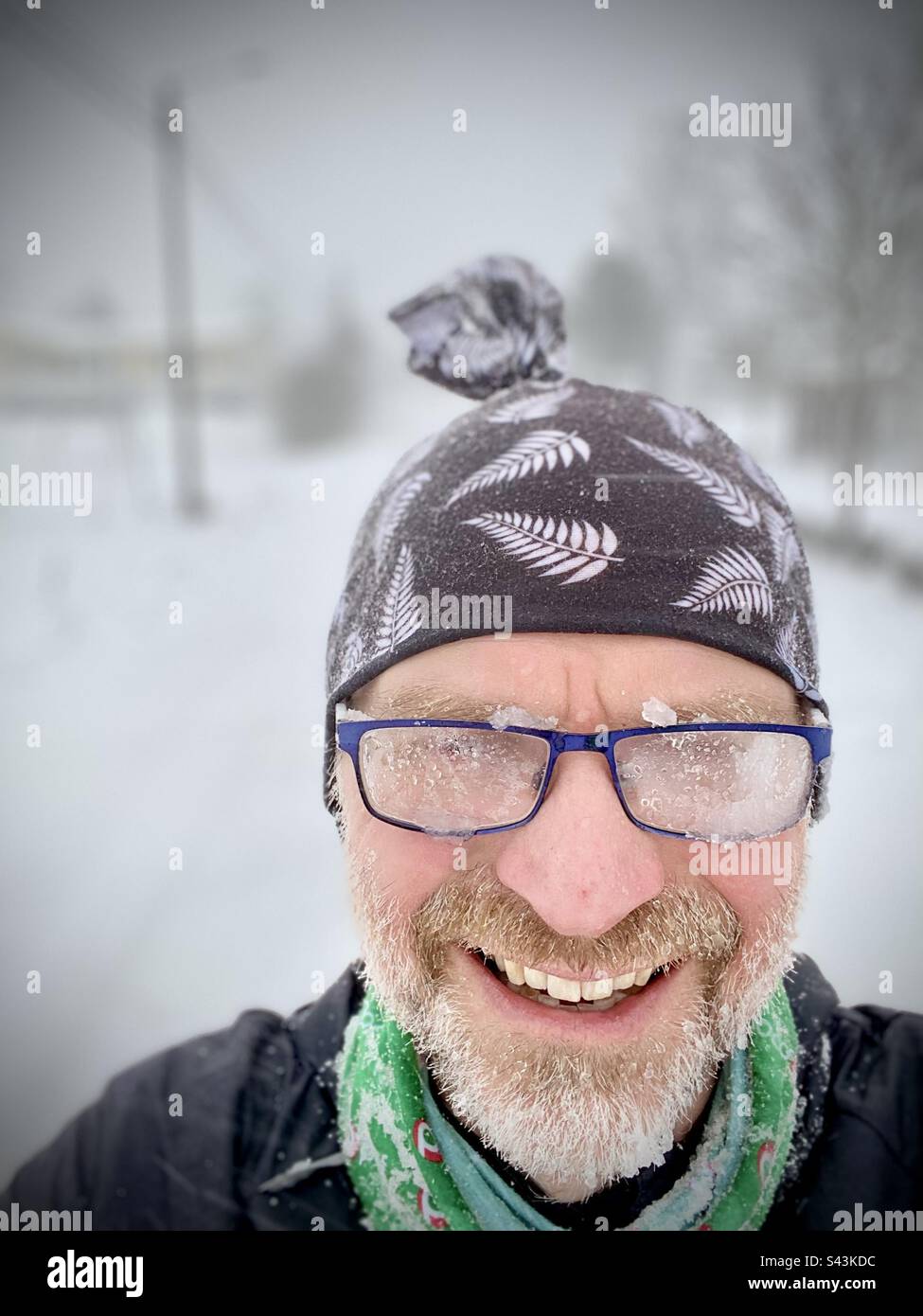 A funny selfie of a middle age man with steamed up glasses covered in sleet and an ice beard after running in a snowstorm during winter in Finland Stock Photo