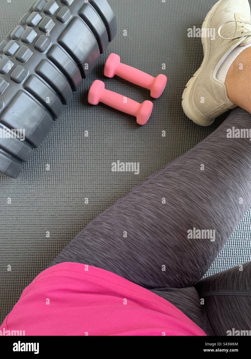 Closeup image of a lady about to begin a gym workout using a mat, a back roller and a pair of dumbbells - Smartphone Captured Stock Image