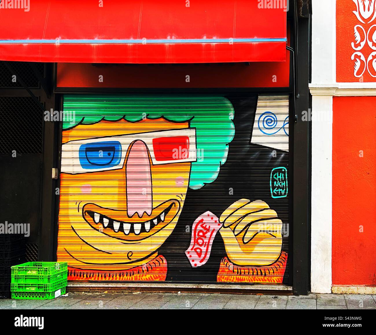 Colourful shutter art on a shop front portrays a person’s face with a broad smile and wearing glasses. The person is waving a note in the left hand - Smartphone Captured Stock Image