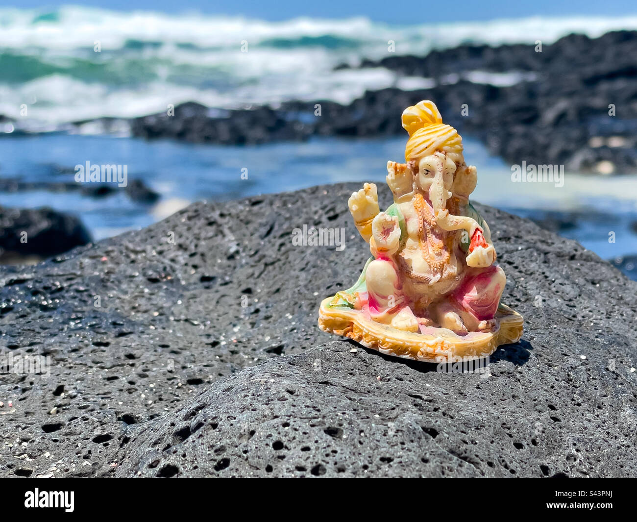 Figure of Hindu God Ganesh placed on rocks at Roche Noires beach, Poste de Flacq, Mauritius, Africa - Smartphone Captured Stock Image