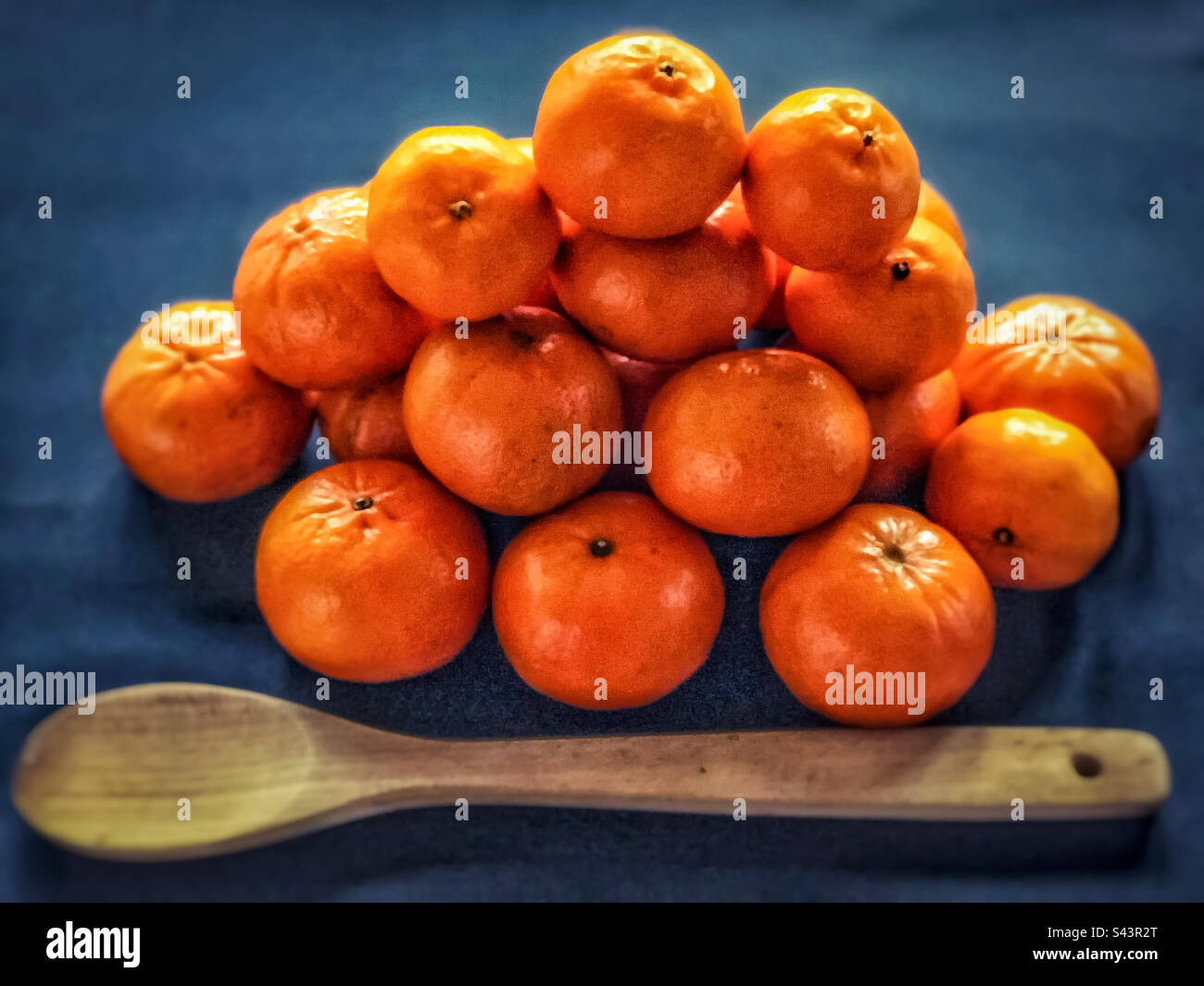 High angle view of a heap of oranges with a big wooden spoon on dark blue background. - Smartphone Captured Stock Image