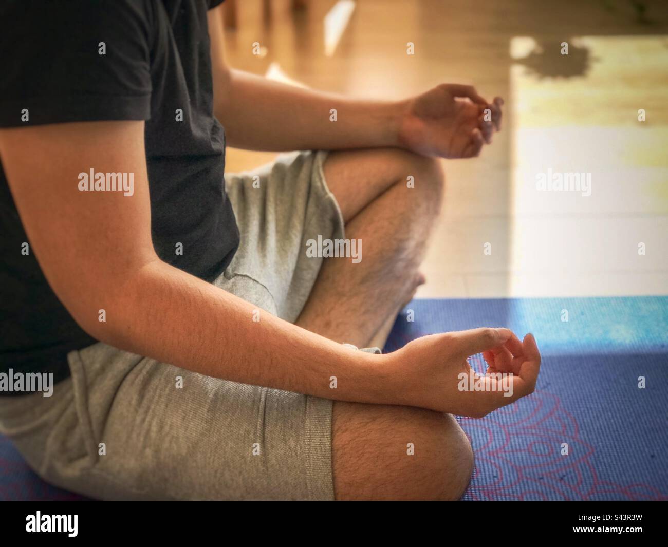 Midsection and low section of young adult man sitting cross legged on yoga mat, meditating after finishing yoga session. - Smartphone Captured Stock Image