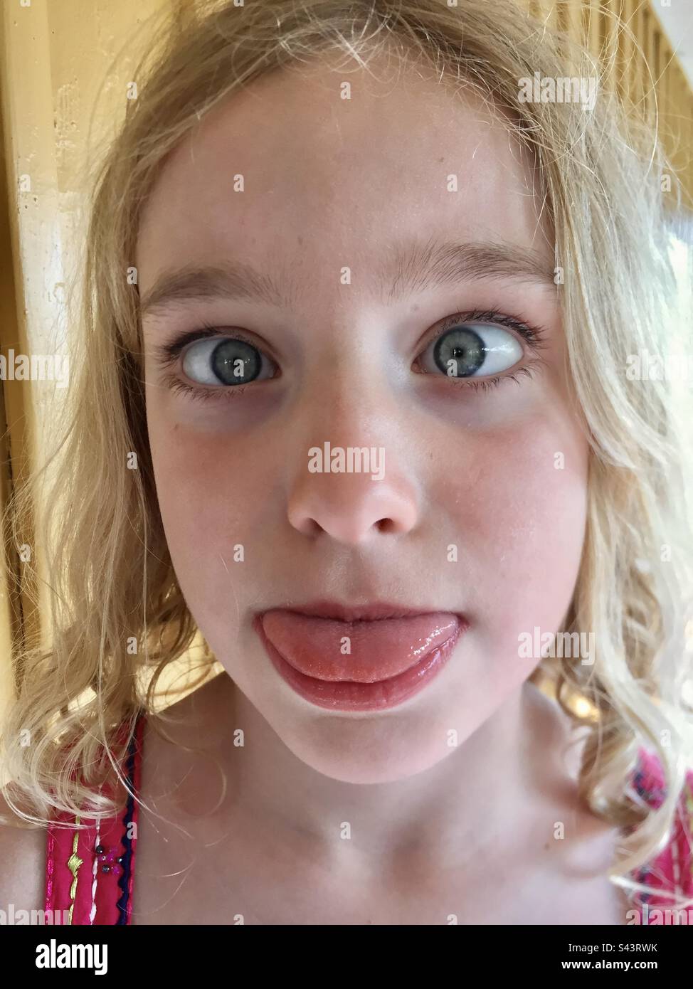 A young 7-year-old girl on messing about crossing her eyes and poking tongue out sticking tongue out making a face Stock Photo