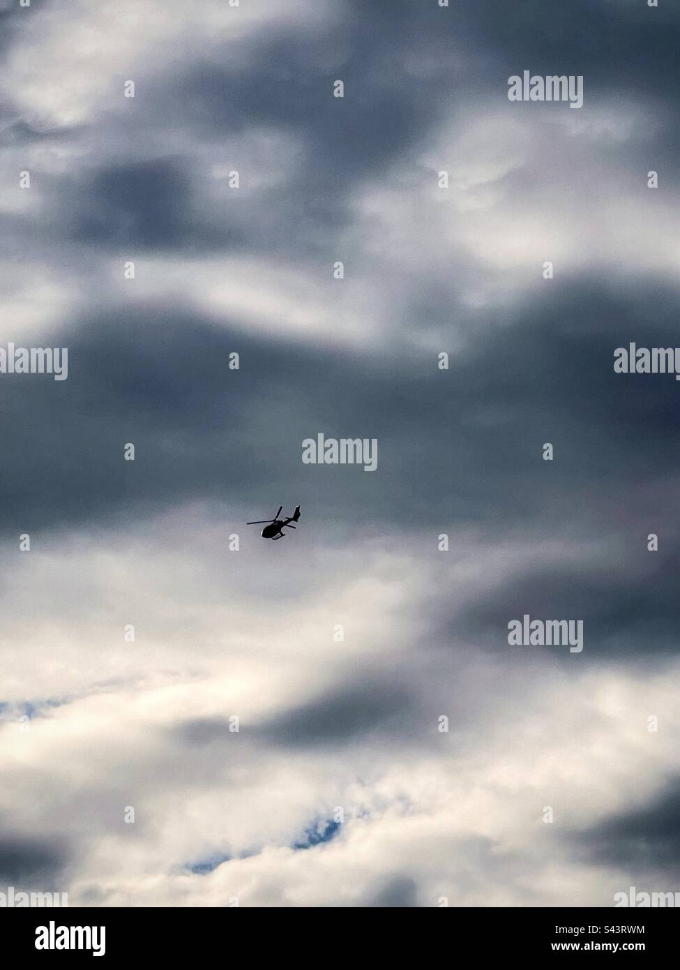 Low angle view of a helicopter flying against cloudy dramatic sky. Stock Photo