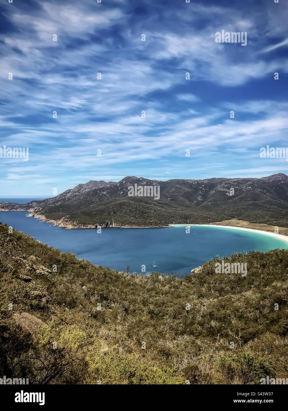 Scenic view of sea, bay, white curving beach surrounded by hills under blue cloudy sky, Wineglass Bay in Freycinet National Park, Tasmania, Australia. - Smartphone Captured Stock Image