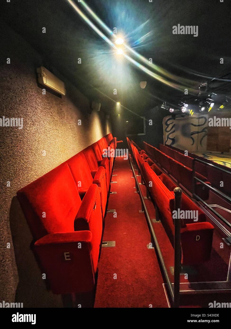 Row of red velvet seats in the small Jermyn Street Theatre near Piccadilly in London. Inside the auditorium or performance space. Stage is set for a play. - Smartphone Captured Stock Image