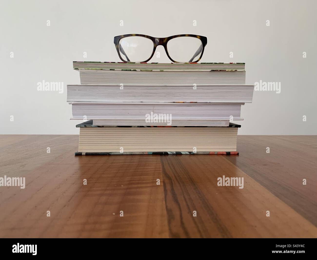 Closeup image of a pile of books on a wooden table against a white background - Smartphone Captured Stock Image