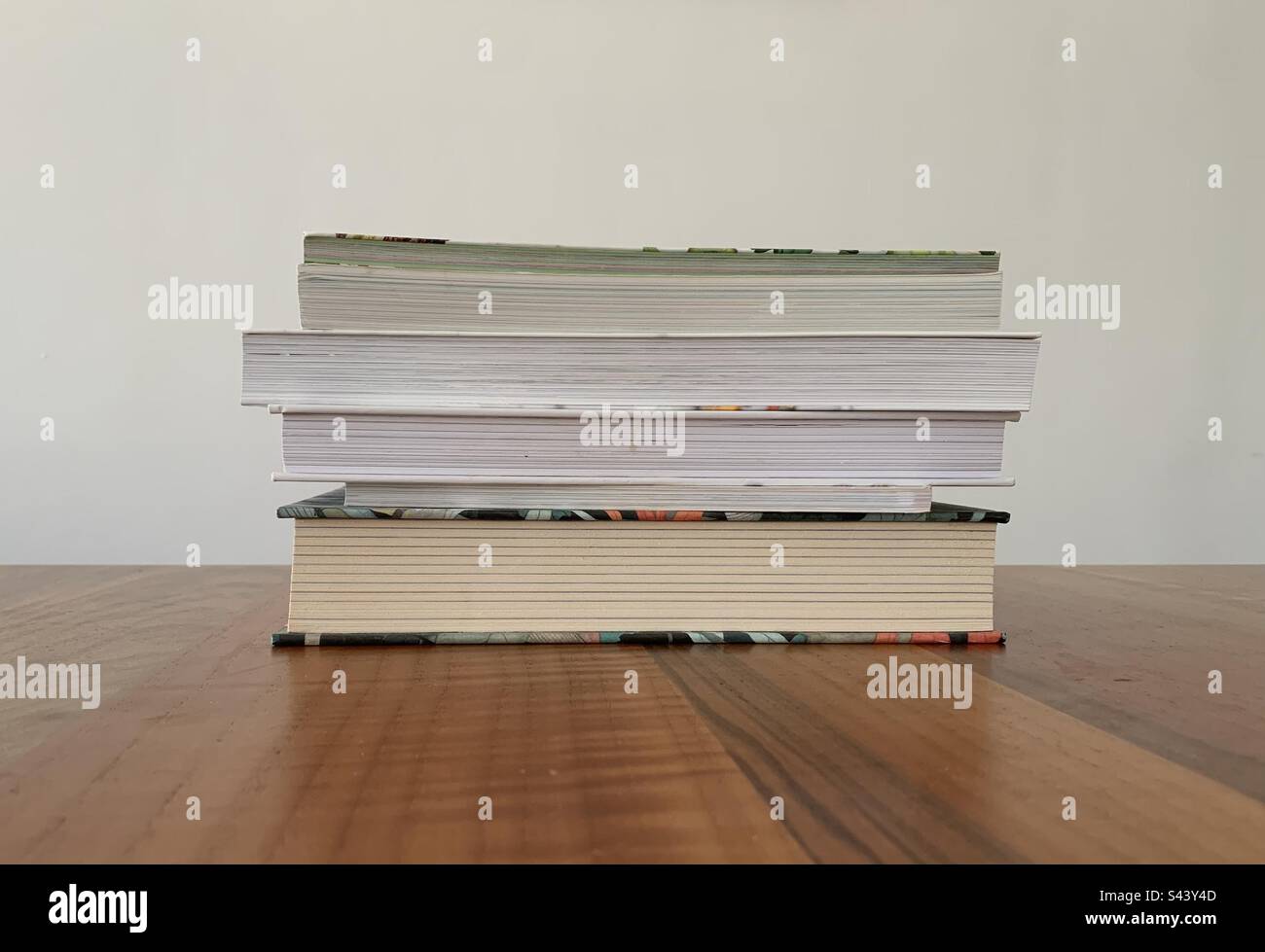 Closeup image of a pile of books on a wooden table against a white background - Smartphone Captured Stock Image