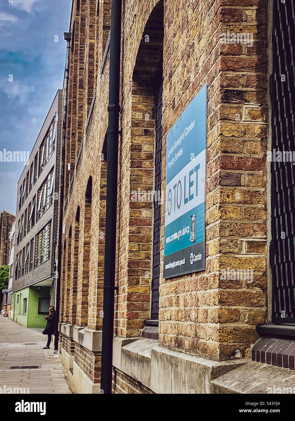 A man takes a break in the sun by a building in London UK - Smartphone Captured Stock Image