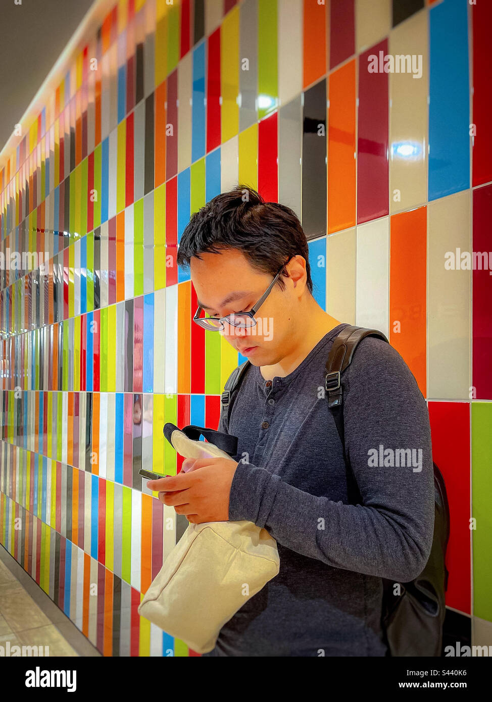 Young Asian man using mobile phone while standing against colorful tiled wall. - Smartphone Captured Stock Image