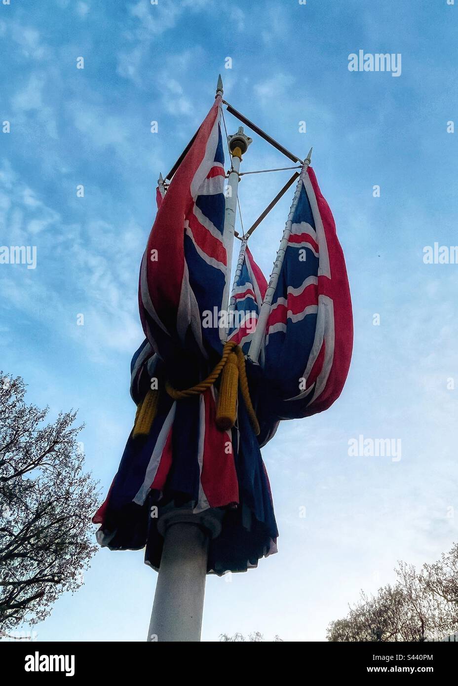 The Union Jack or union flag of the United Kingdom is on a flag staff in The Mall in London- folded ready for the coronation of King Charles III - on top is a newly painted crown Stock Photo