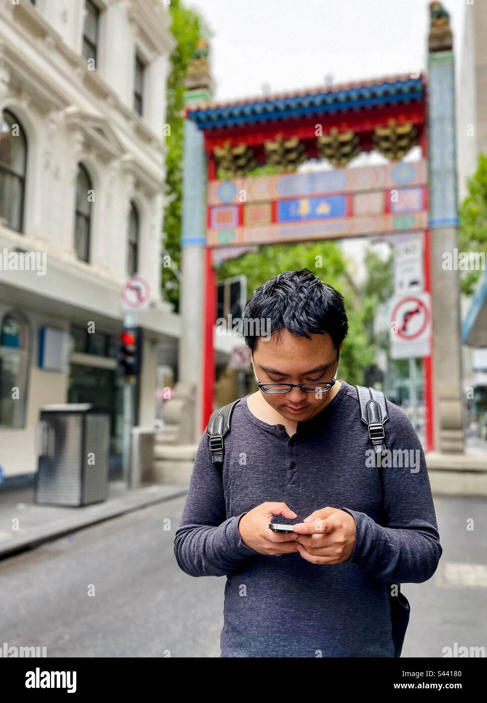 Young Asian man using smartphone while standing on the street against arch and buildings in Chinatown, Melbourne, Australia. - Smartphone Captured Stock Image