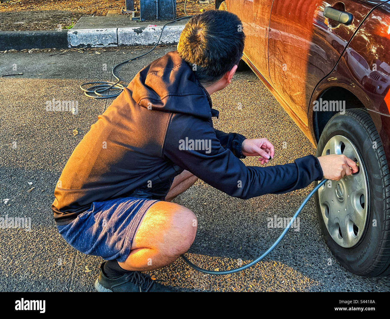 Side view of young adult man using tyre pump at petrol station to inflate tyre of car. - Smartphone Captured Stock Image